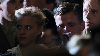 Movie still from “Memphis Belle” (1990), directed by Michael Caton-Jones – A man and a woman sitting next to each other in a crowd; Close Up shot, Low angle