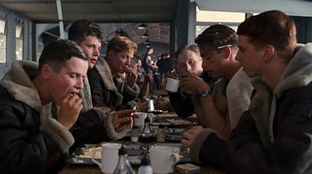 Movie still from “Memphis Belle” (1990), directed by Michael Caton-Jones – A group of people sitting at a table eating food; Medium shot, Over the shoulder angle
