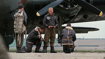 Movie still from “Memphis Belle” (1990), directed by Michael Caton-Jones – A group of men standing around a plane; Wide shot, Low angle