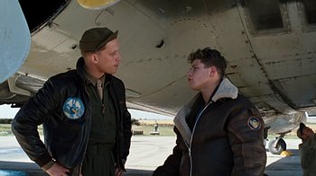 Movie still from “Memphis Belle” (1990), directed by Michael Caton-Jones – Two young men are standing in front of an airplane; Medium shot, Over the shoulder angle