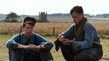 Movie still from “Memphis Belle” (1990), directed by Michael Caton-Jones – Two men sitting in a field looking at their cell phones; Medium shot, Over the shoulder angle