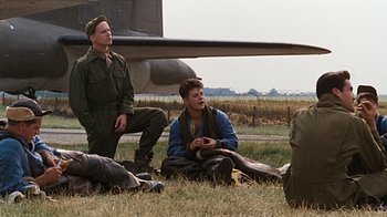 Movie still from “Memphis Belle” (1990), directed by Michael Caton-Jones – A group of men sitting on the ground next to an airplane; Wide shot, Low angle