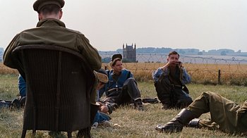 Movie still from “Memphis Belle” (1990), directed by Michael Caton-Jones – A group of men sitting on the ground in a field; Wide shot, Over the shoulder angle