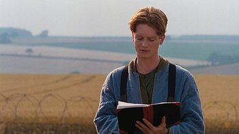 Movie still from “Memphis Belle” (1990), directed by Michael Caton-Jones – A man standing in a field reading a book; Medium shot, Low angle