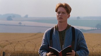 Movie still from “Memphis Belle” (1990), directed by Michael Caton-Jones – A man holding a book while standing in a field; Medium shot, Low angle