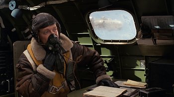 Movie still from “Memphis Belle” (1990), directed by Michael Caton-Jones – A man in a fighter pilot's uniform is sitting in the cockpit of an aircraft; Medium shot, Low angle