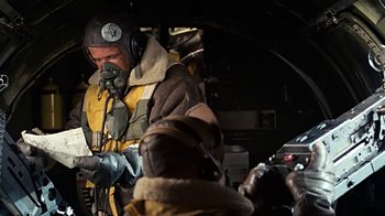 Movie still from “Memphis Belle” (1990), directed by Michael Caton-Jones – A man in a yellow and black jacket is looking at his cell phone; Medium shot, Low angle