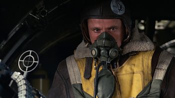 Movie still from “Memphis Belle” (1990), directed by Michael Caton-Jones – A man in a yellow jacket wearing a gas mask; Close Up shot, Low angle