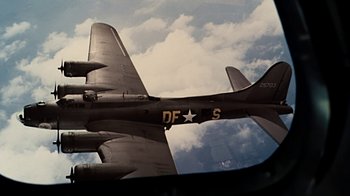 Movie still from “Memphis Belle” (1990), directed by Michael Caton-Jones – A fighter jet flying through a cloudy blue sky; Wide shot, Low angle