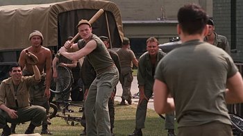 Movie still from “Memphis Belle” (1990), directed by Michael Caton-Jones – A man holding a baseball bat while standing next to a group of men; Medium shot, Over the shoulder angle