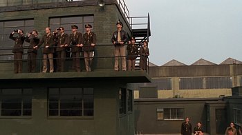 Movie still from “Memphis Belle” (1990), directed by Michael Caton-Jones – A group of men standing on top of a green building; Wide shot, Low angle