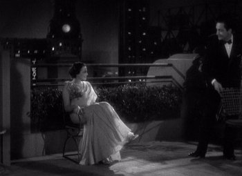 Movie still from “Merrily We Go to Hell” (1932), directed by Dorothy Arzner – A woman sitting on top of a chair next to a man; Wide shot, High angle