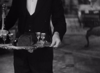 Movie still from “Merrily We Go to Hell” (1932), directed by Dorothy Arzner – A man in a tuxedo holding a tray of food and two glasses; Medium shot, High angle