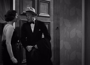 Movie still from “Merrily We Go to Hell” (1932), directed by Dorothy Arzner – A man in a suit and hat talking to a woman; Medium shot, Over the shoulder angle