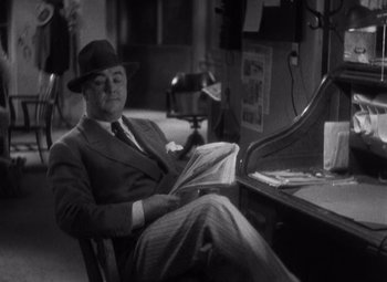 Movie still from “Merrily We Go to Hell” (1932), directed by Dorothy Arzner – A black and white photo of a man sitting at a desk; Medium shot, High angle