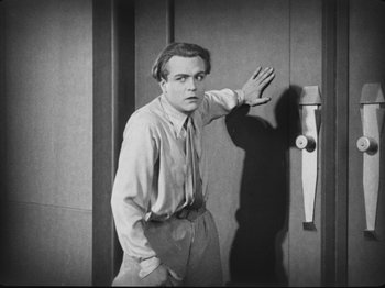 Movie still from “Metropolis” (1927), directed by Fritz Lang – A black and white photo of a man leaning against a door; Medium shot, High angle