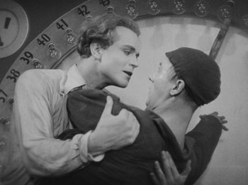 Movie still from “Metropolis” (1927), directed by Fritz Lang – Two men embracing each other in front of a clock tower; Medium shot, Low angle