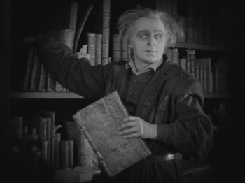 Movie still from “Metropolis” (1927), directed by Fritz Lang – A man holding an old book in a library; Medium shot, High angle