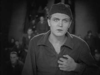 Movie still from “Metropolis” (1927), directed by Fritz Lang – A man with a hat on is holding his chest; Close Up shot, High angle