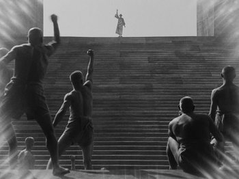 Movie still from “Metropolis” (1927), directed by Fritz Lang – A group of men standing on top of a set of stairs; Extreme Wide shot, Low angle