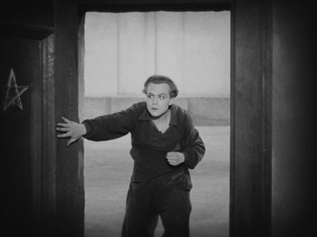 Movie still from “Metropolis” (1927), directed by Fritz Lang – A black and white photo of a man standing in an open doorway; Medium shot, High angle