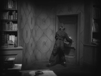 Movie still from “Metropolis” (1927), directed by Fritz Lang – A man standing in front of an open door in a room; Wide shot, High angle