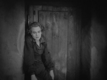 Movie still from “Metropolis” (1927), directed by Fritz Lang – A woman sitting in a doorway wearing a black suit; Medium shot, High angle