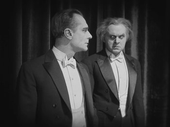 Movie still from “Metropolis” (1927), directed by Fritz Lang – A couple of men standing next to each other in tuxedos; Medium shot, Over the shoulder angle