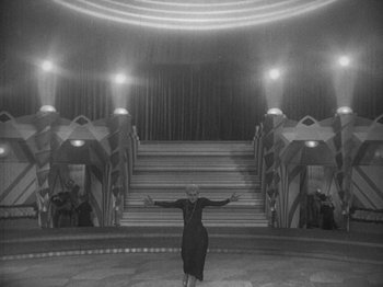 Movie still from “Metropolis” (1927), directed by Fritz Lang – An old photo of a woman standing in front of a staircase; Extreme Wide shot, High angle