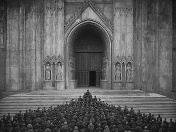 Movie still from “Metropolis” (1927), directed by Fritz Lang – A black and white photo of a group of people sitting in front of a building; Extreme Wide shot, High angle