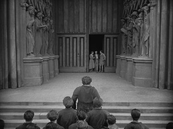 Movie still from “Metropolis” (1927), directed by Fritz Lang – A group of people standing on steps in front of a building; Extreme Wide shot, High angle