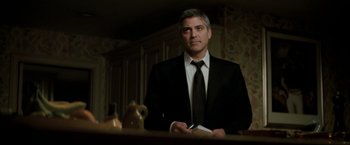 Movie still from “Michael Clayton” (2007), directed by Tony Gilroy – A man wearing a suit and tie holding a book; Medium shot, Low angle
