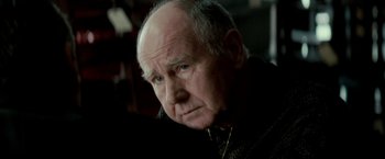 Movie still from “Michael Clayton” (2007), directed by Tony Gilroy – An older man with a beard and a necklace; Close Up shot, Over the shoulder angle