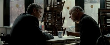 Movie still from “Michael Clayton” (2007), directed by Tony Gilroy – Two people sitting at a table in front of each other; Medium shot, Over the shoulder angle