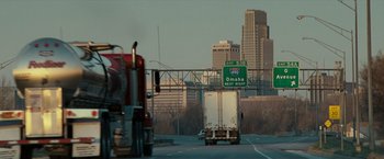 Movie still from “Michael Clayton” (2007), directed by Tony Gilroy – A truck driving down a street with a sign on the side of the road; Extreme Wide shot, Over the shoulder angle