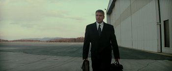 Movie still from “Michael Clayton” (2007), directed by Tony Gilroy – A man in a suit and tie holding two briefcases; Medium shot, Low angle