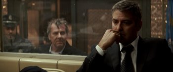 Movie still from “Michael Clayton” (2007), directed by Tony Gilroy – A man in a suit sitting next to another man in a suit; Close Up shot, Over the shoulder angle