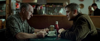 Movie still from “Michael Clayton” (2007), directed by Tony Gilroy – Two men sitting at a table in front of a cup of coffee; Medium shot, Over the shoulder angle