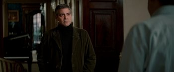 Movie still from “Michael Clayton” (2007), directed by Tony Gilroy – A man standing in front of a door wearing a jacket; Medium shot, Over the shoulder angle