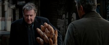 Movie still from “Michael Clayton” (2007), directed by Tony Gilroy – A man in a black suit holding a bunch of potatoes; Close Up shot, Over the shoulder angle