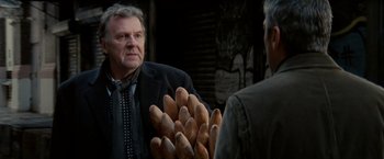Movie still from “Michael Clayton” (2007), directed by Tony Gilroy – A man in a suit and tie holding a bunch of food; Close Up shot, Over the shoulder angle