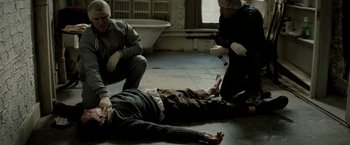 Movie still from “Michael Clayton” (2007), directed by Tony Gilroy – A man is lying on the ground while two other men watch; Medium shot, High angle