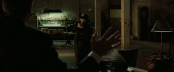 Movie still from “Michael Clayton” (2007), directed by Tony Gilroy – A man holding a gun in a room with people clapping in front of him; Medium shot, Over the shoulder angle