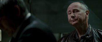 Movie still from “Michael Clayton” (2007), directed by Tony Gilroy – An older man wearing a brown leather jacket; Close Up shot, Over the shoulder angle