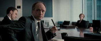 Movie still from “Michael Clayton” (2007), directed by Tony Gilroy – A man in a suit and tie holding a pair of glasses; Close Up shot, Low angle