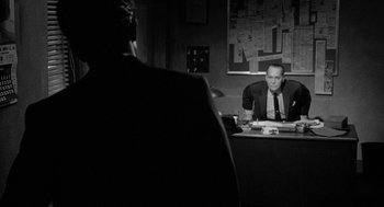 Movie still from “Mickey One” (1965), directed by Arthur Penn – A man sitting at a desk in front of a mirror; Medium shot, Over the shoulder angle