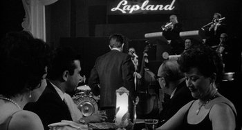 Movie still from “Mickey One” (1965), directed by Arthur Penn – A black and white photo of people at an event; Wide shot, Over the shoulder angle