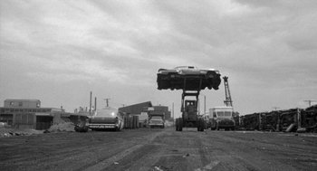 Movie still from “Mickey One” (1965), directed by Arthur Penn – A black and white photo of cars being lifted by a crane; Wide shot, Low angle