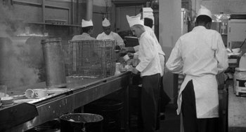 Movie still from “Mickey One” (1965), directed by Arthur Penn – A black and white photo of a chef preparing food in a restaurant kitchen; Medium shot, High angle