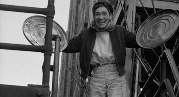 Movie still from “Mickey One” (1965), directed by Arthur Penn – An old black and white photo of a man smiling; Medium shot, Low angle